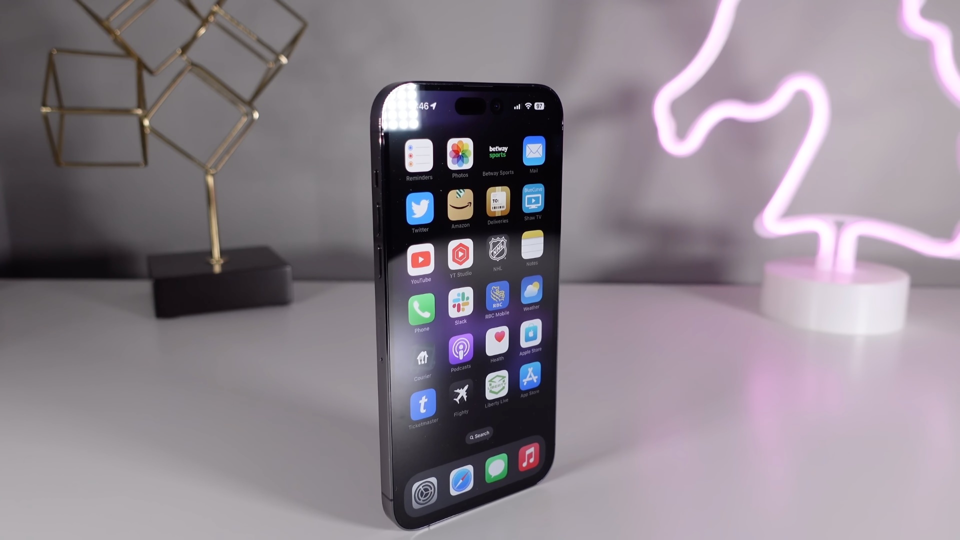 Un Apple iPhone 14 Pro violet foncé posé à la verticale sur un bureau blanc avec un éclairage d'ambiance au néon en arrière-plan