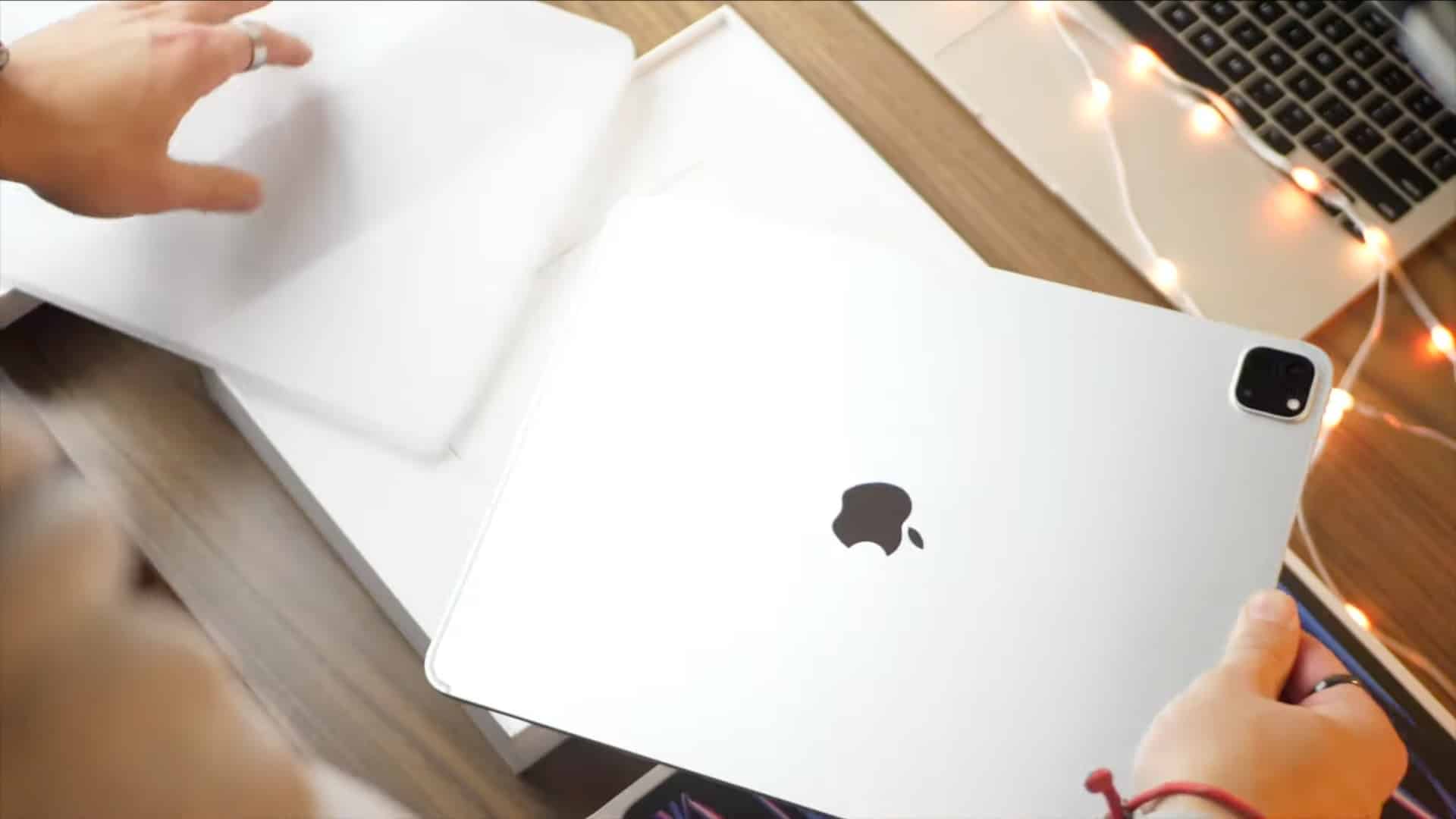 Les mains d'un jeune homme au-dessus d'un bureau en bois retirant l'emballage en plastique d'un tout nouvel iPad Pro 12,9 pouces 